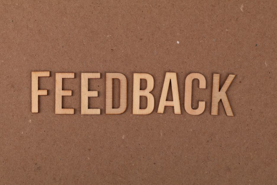 A close-up of a wooden 'FEEDBACK' sign on a textured cardboard background.